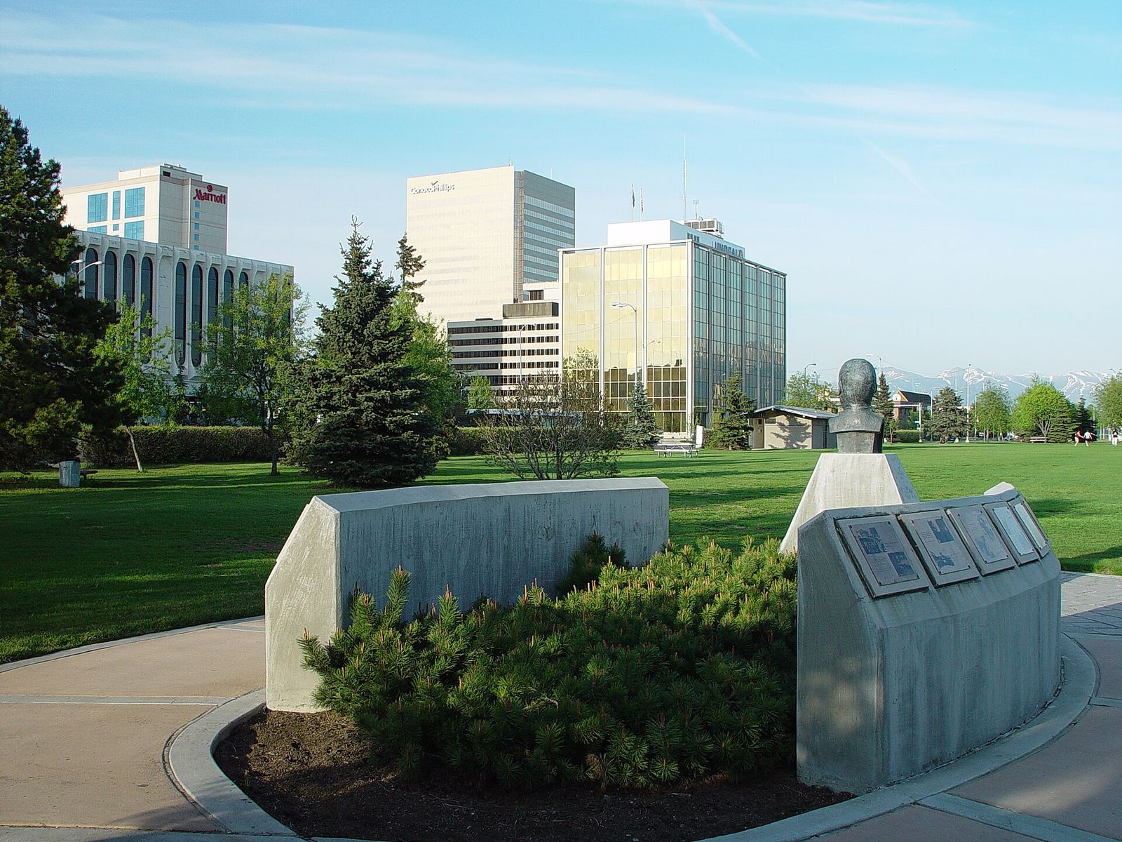 Downtown Anchorage office buildings seen from the lawn and stone monuments of the Delaney Park Strip