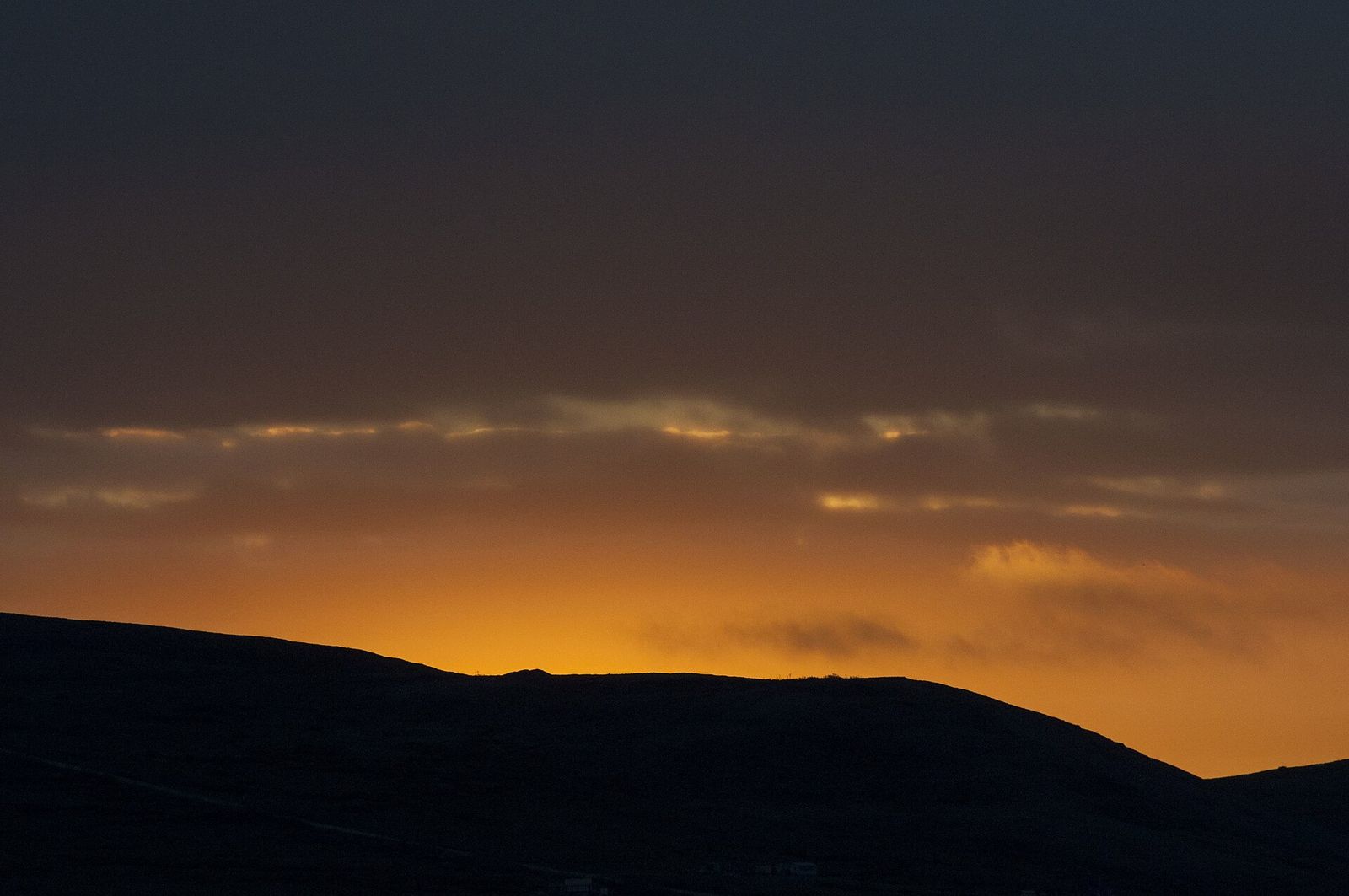 Orange light along the horizon above dark hills at sunrise near the summer solstice in the Nome area
