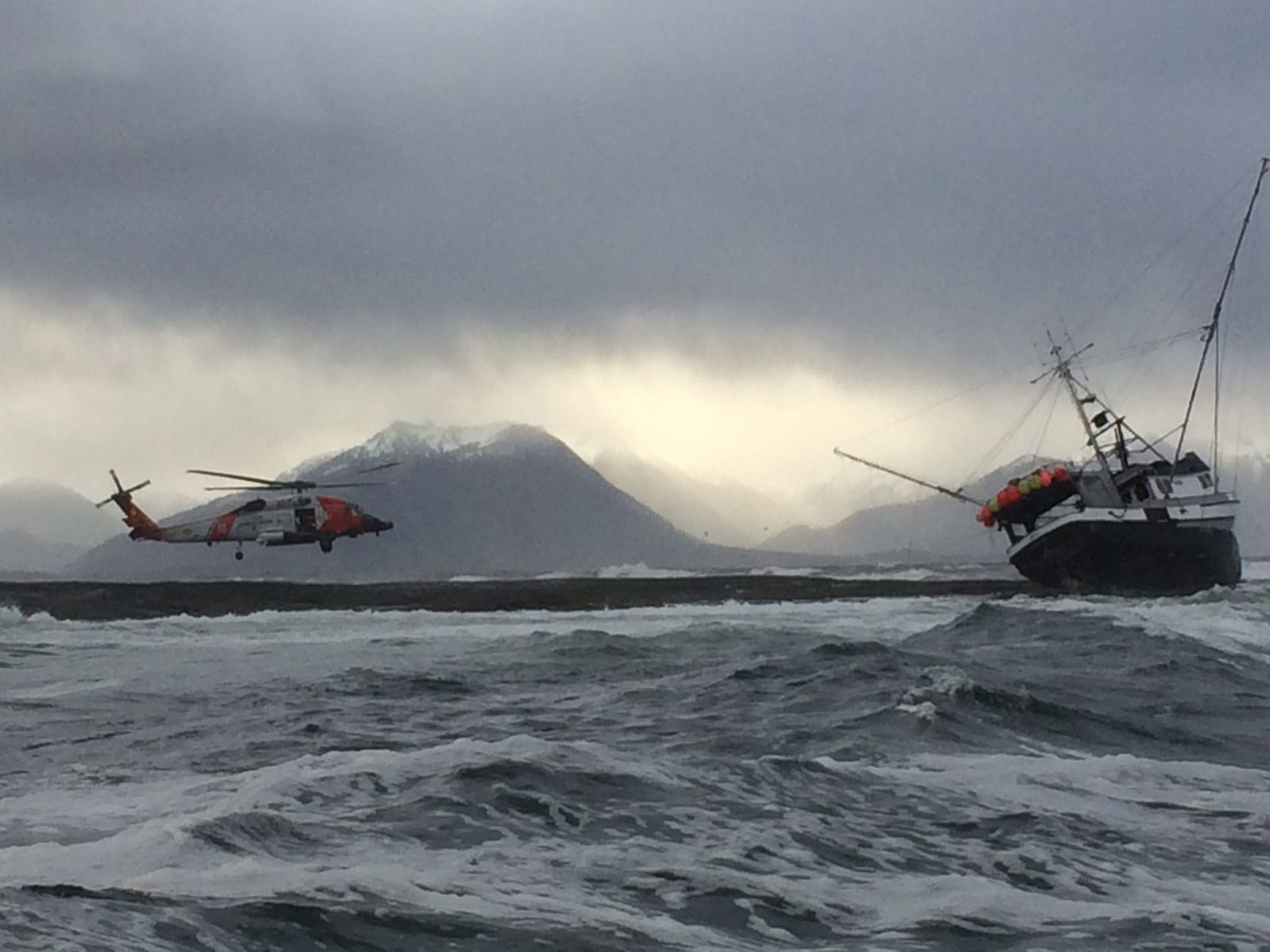 A Coast Guard MH-60 Jayhawk helicopter from Air Station Sitka flying over rough seas near a fishing vessel