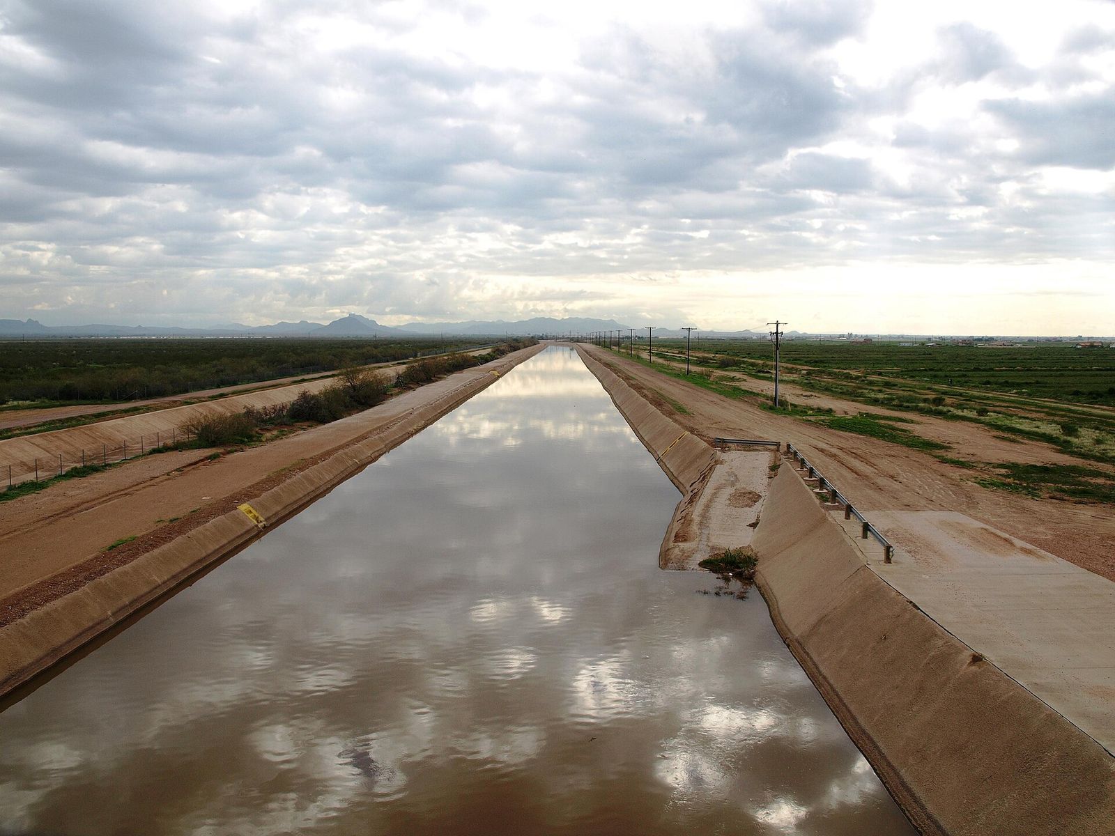 The Arizona Canal of the Salt River Project running straight through flat farmland in Maricopa County under a cloudy sky