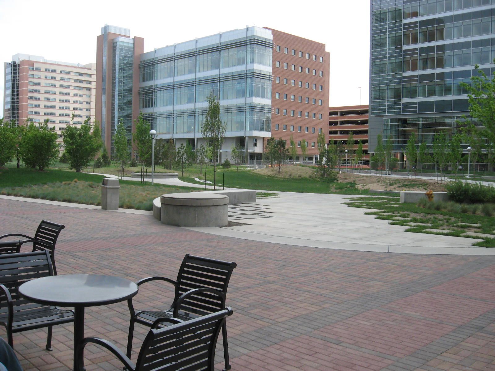 A brick plaza with outdoor tables and chairs in front of glass and brick buildings on the Anschutz Medical Campus in Aurora, Colorado