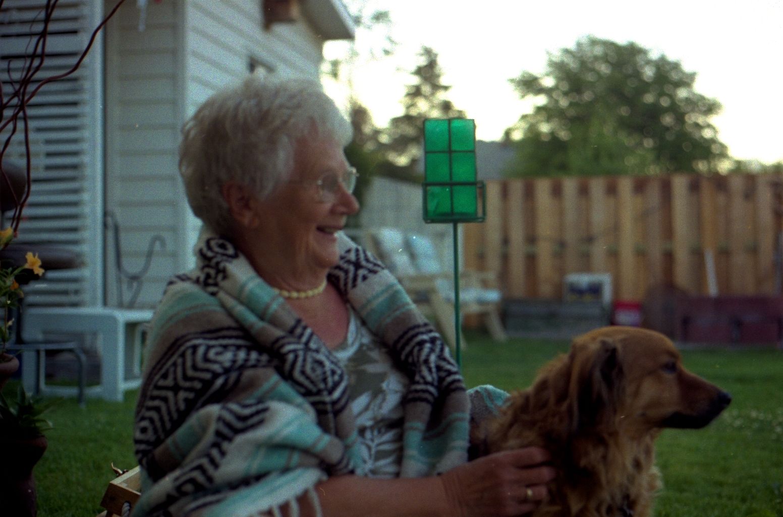 A smiling older woman sitting outdoors with her golden retriever