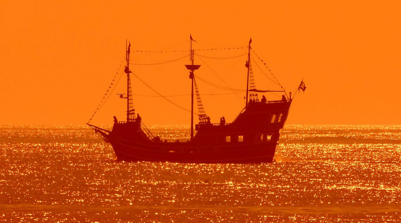 A pirate-themed excursion ship silhouetted on the Gulf at sunset