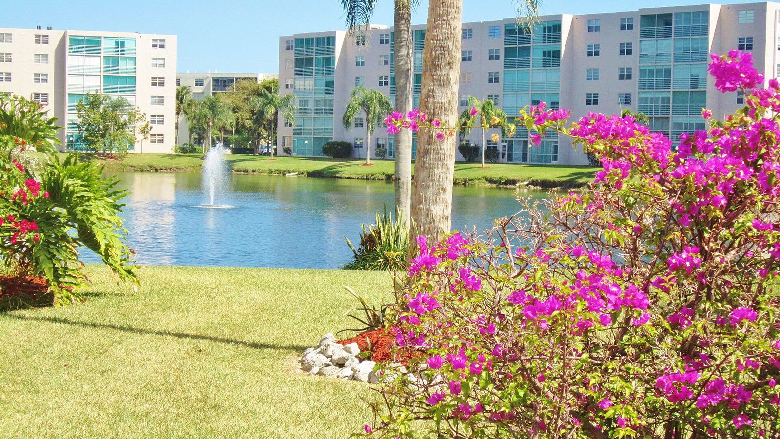 A Florida condominium beside a lake with a fountain and flowering shrubs