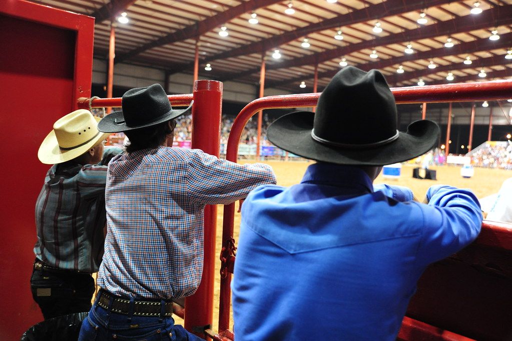 Cowboys in hats watching the action from the rails at a rodeo arena