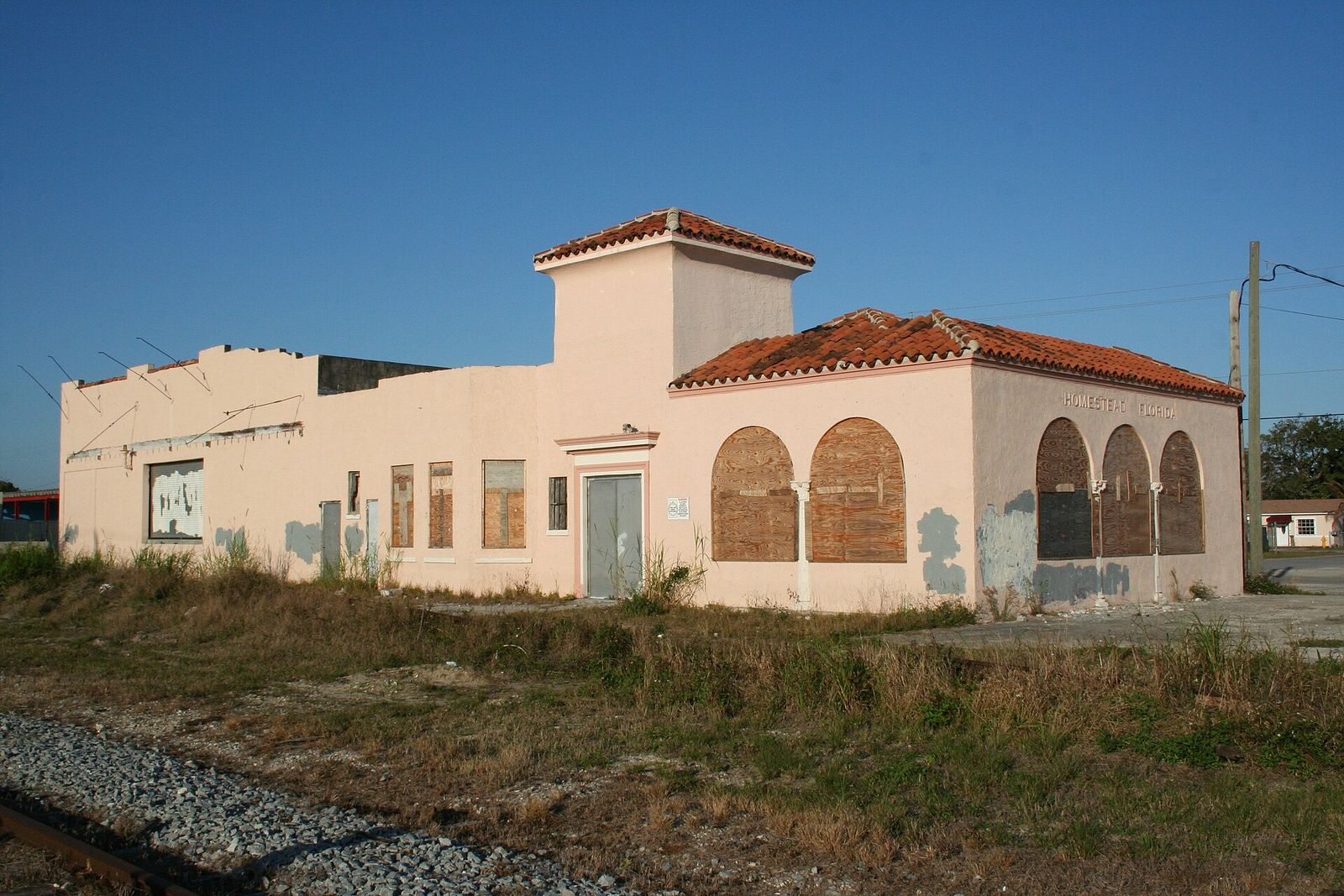 The old Seaboard Air Line Railway station in Homestead, a stucco building with arched, boarded windows beside the tracks