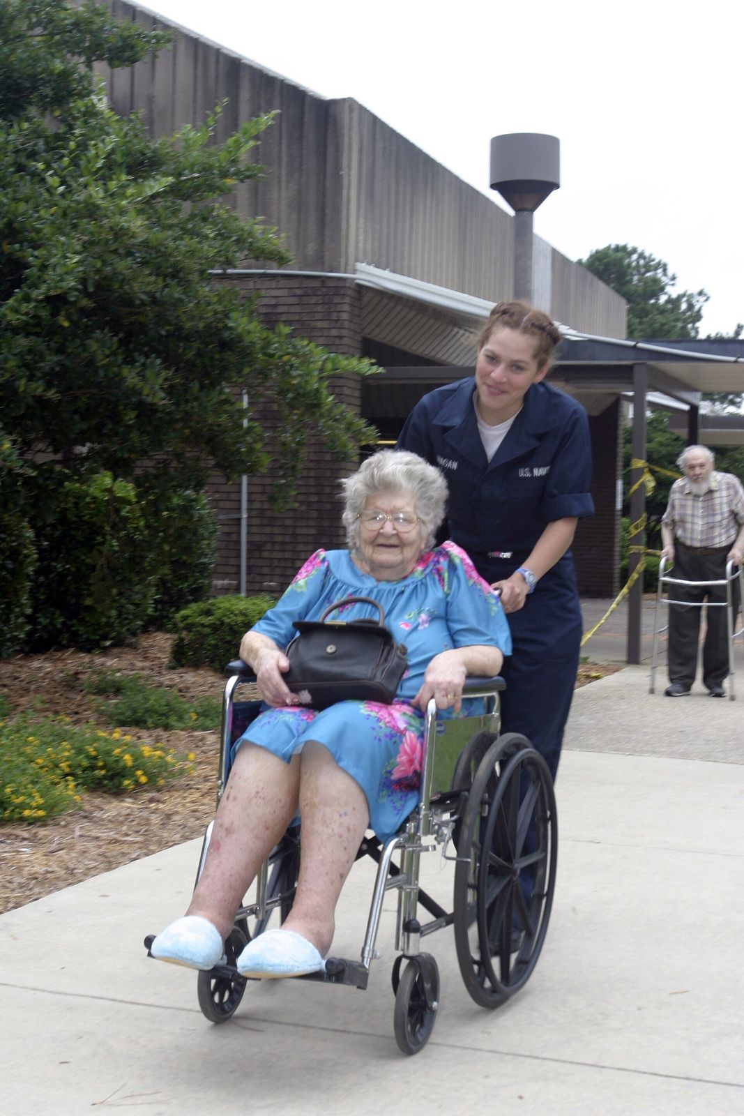 A sailor pushing an elderly woman in a wheelchair during an evacuation