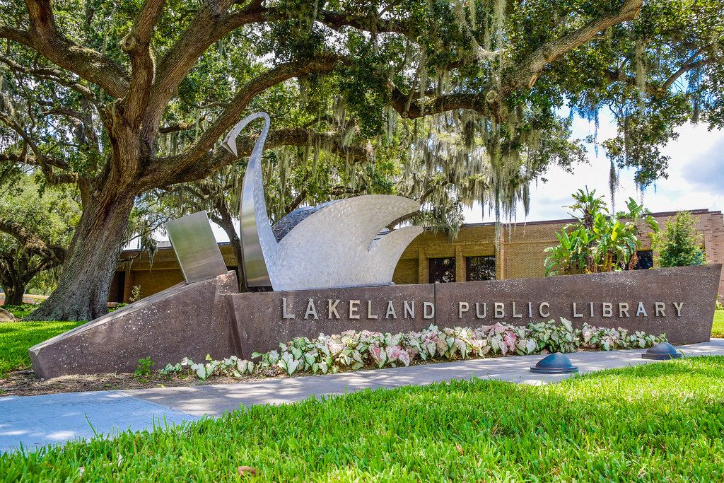 Swan sculpture over the Lakeland Public Library sign under oak trees
