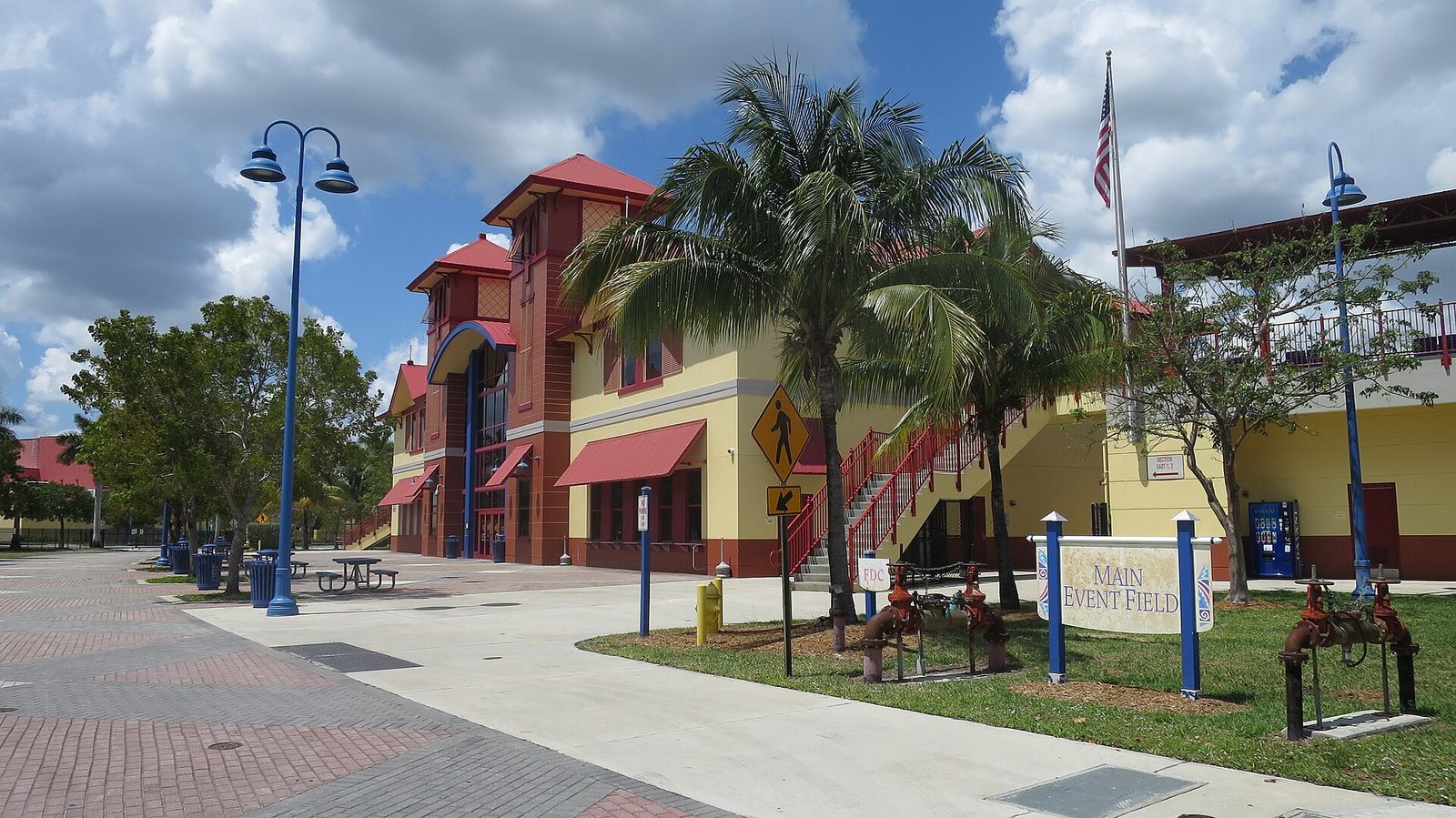 Central Broward Regional Park in Lauderhill, with a paved plaza, palms and the stadium buildings under a cloudy sky
