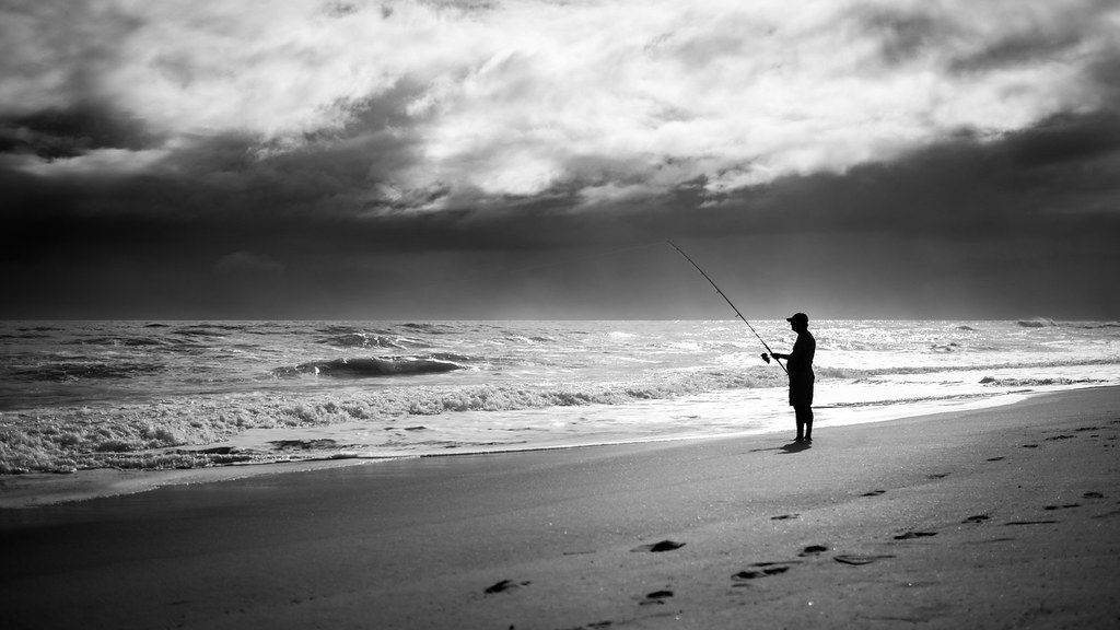 A person fishing from the beach near Melbourne, in black and white