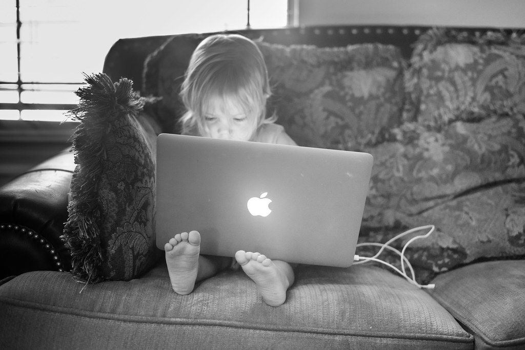 A black and white photo of a dog resting its head by a computer keyboard