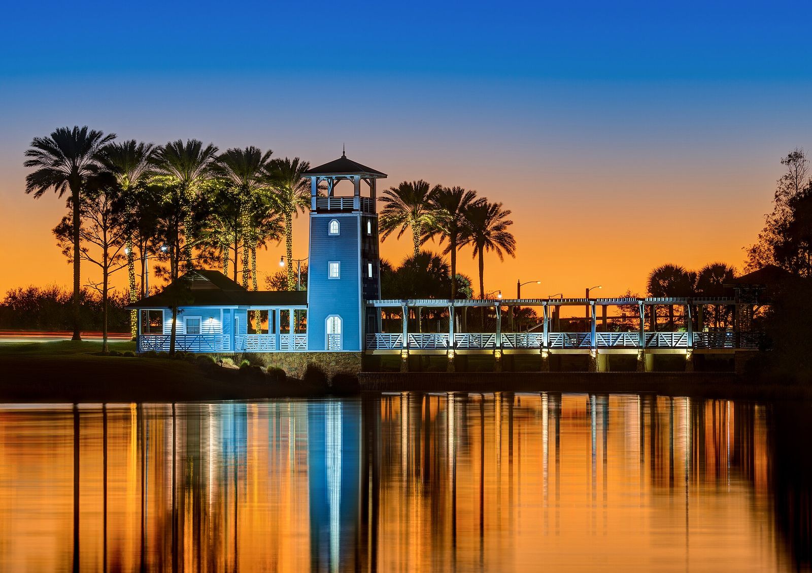 Palm trees and a lit tower reflected in Lake Tradition at twilight