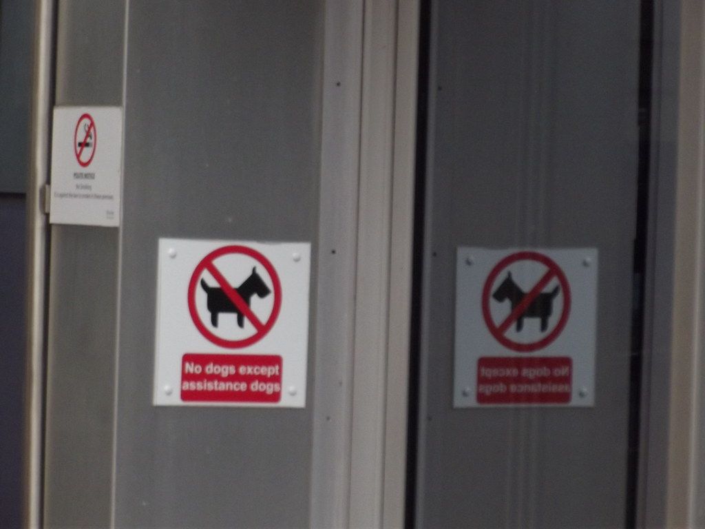 Two no-dogs signs on glass doors with an exception for assistance dogs