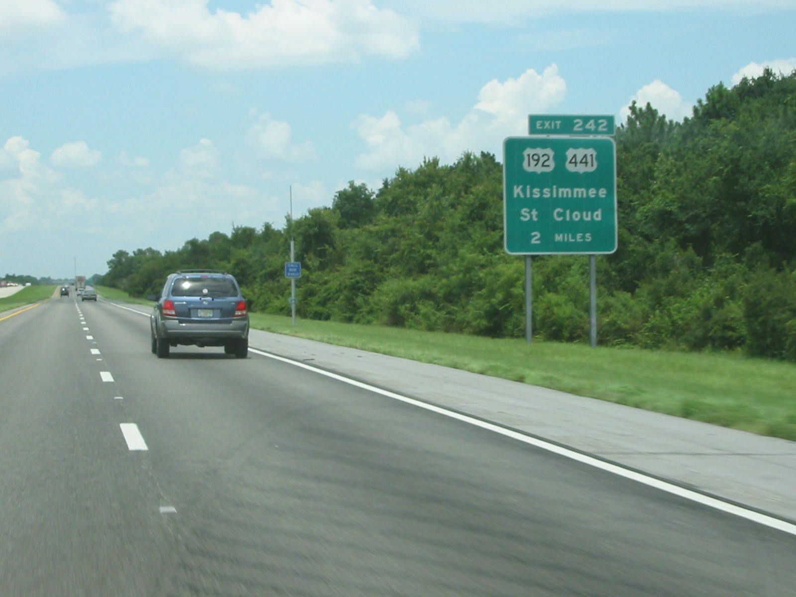 A green Florida's Turnpike sign for exit 242 to U.S. 192 and U.S. 441, Kissimmee and St. Cloud, beside a wooded roadside
