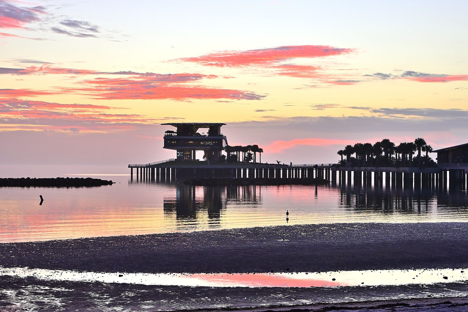 The St. Pete Pier and its head building silhouetted against a pink sunrise over Tampa Bay at low tide