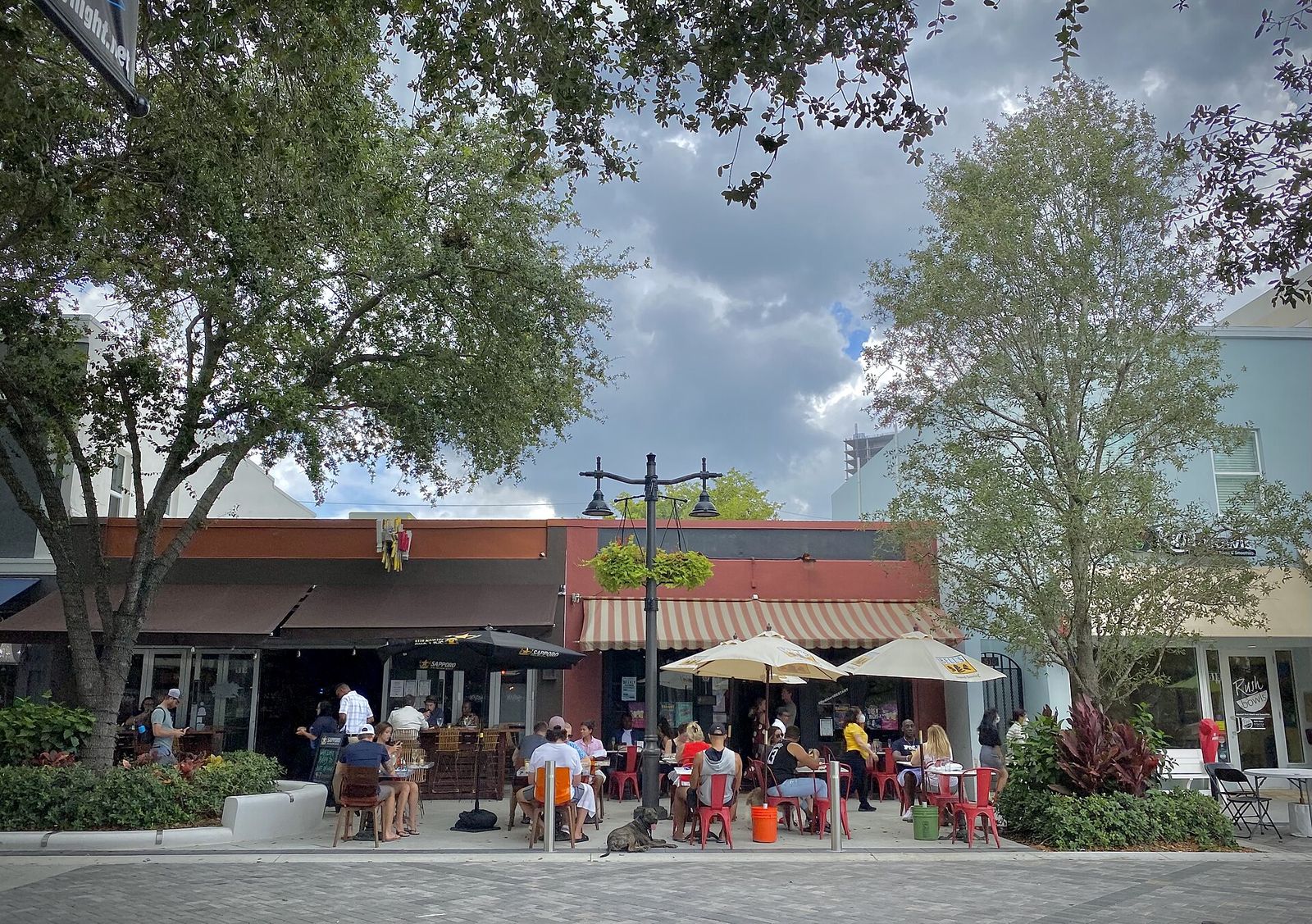 Diners at curbside patio tables under trees on Clematis Street
