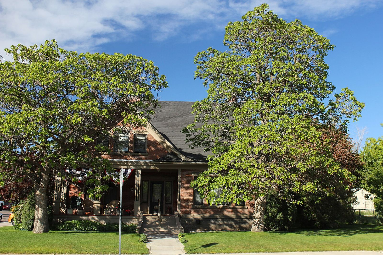 The brick Rice-Packard House in Pocatello, half hidden by tall leafy trees