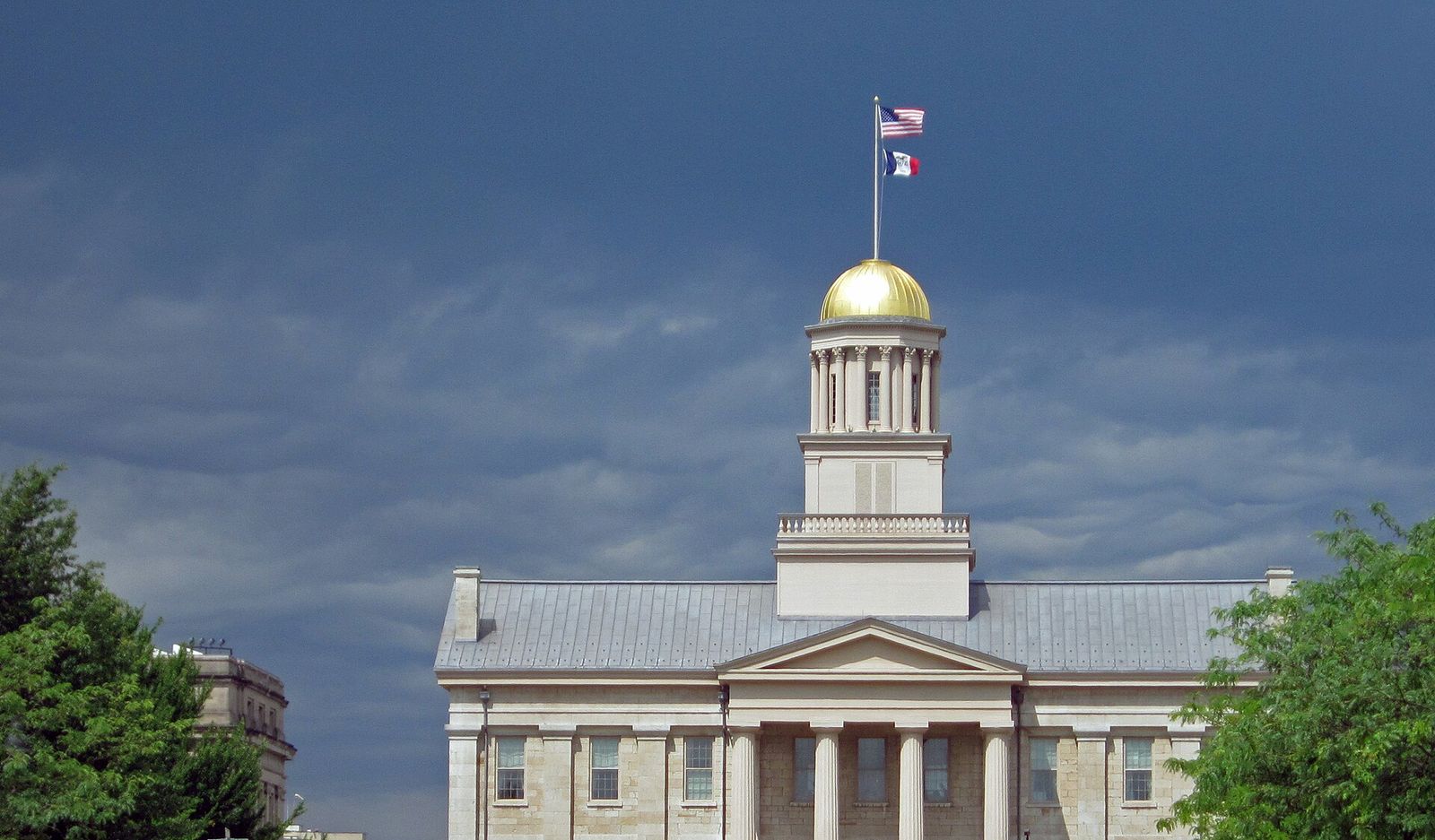The Old Capitol in Iowa City, with its gold dome and white columns, under a dark stormy sky