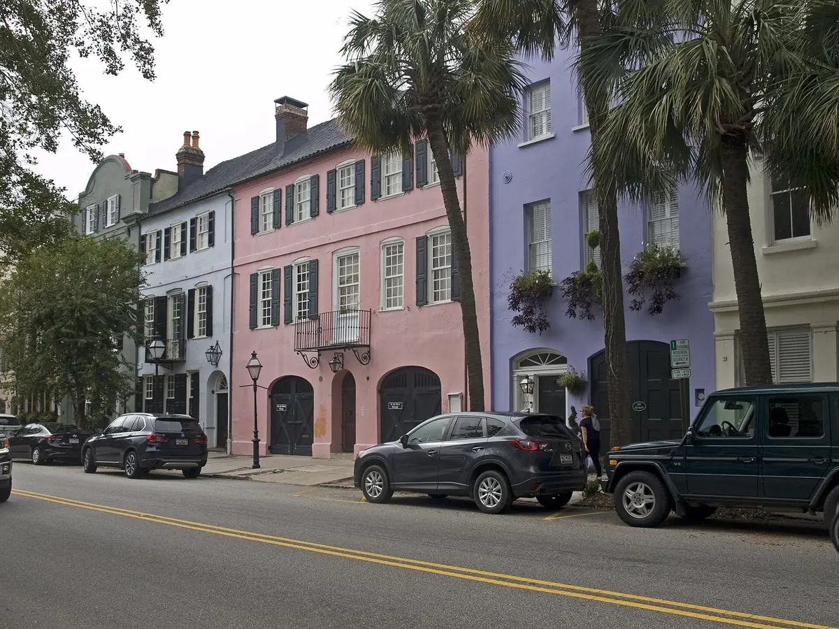 Pink and lavender houses of Rainbow Row on East Bay Street in Charleston, with palmettos and parked cars out front