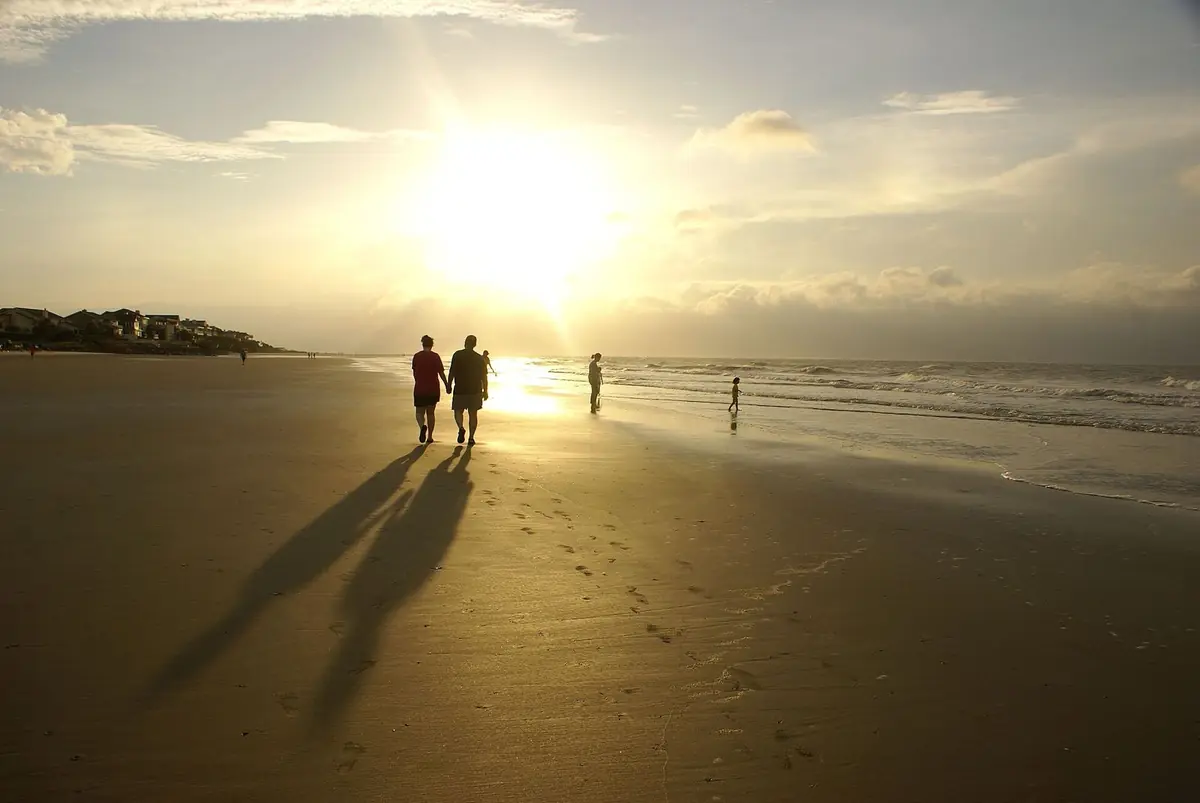 Low sun over the wide beach at Isle of Palms, with people walking along the waterline
