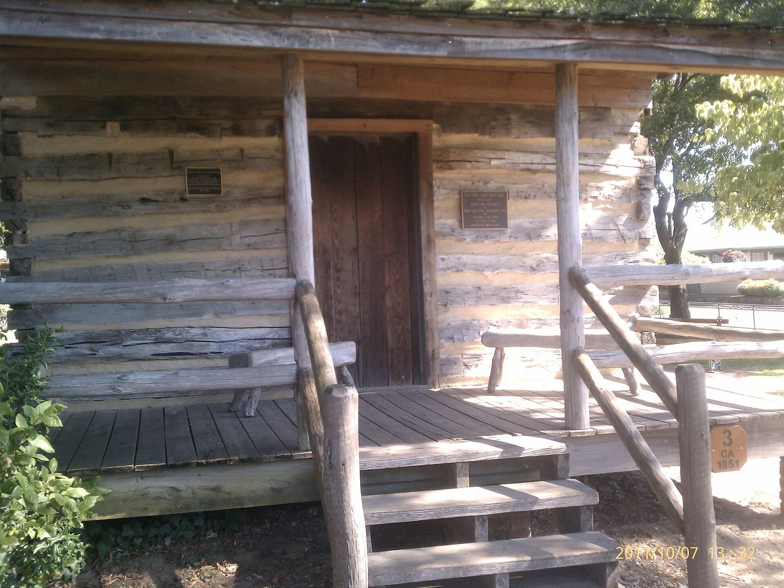 Log cabin with a wooden porch and steps in Collierville's Town Square Park