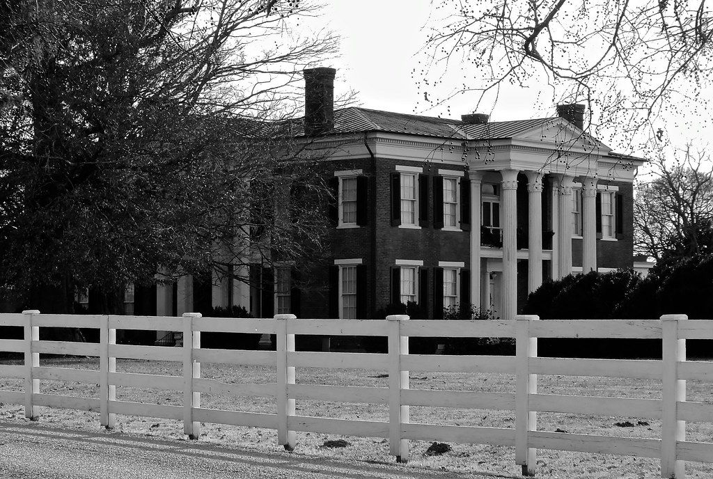 Black and white view of the columned Rippavilla mansion behind a white fence