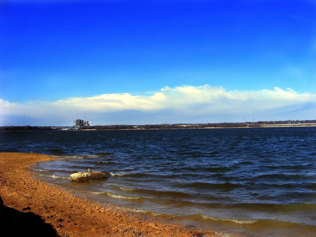 The sandy shore of Lake Arlington, with small waves under a blue sky