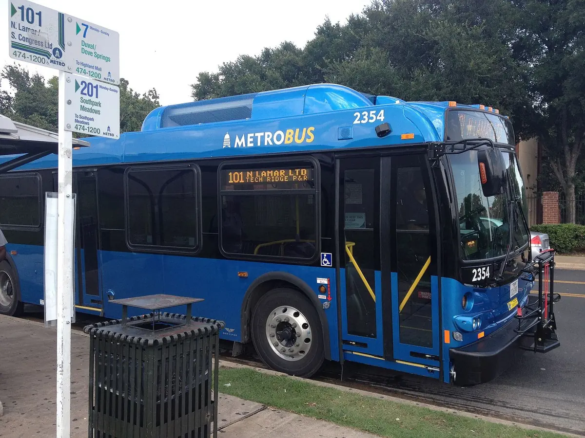 A blue CapMetro MetroBus stopped at a curbside bus stop in Austin