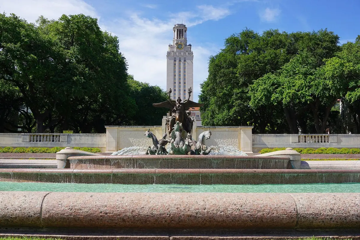A bronze fountain in front of the Main Building tower at the University of Texas at Austin, framed by live oaks