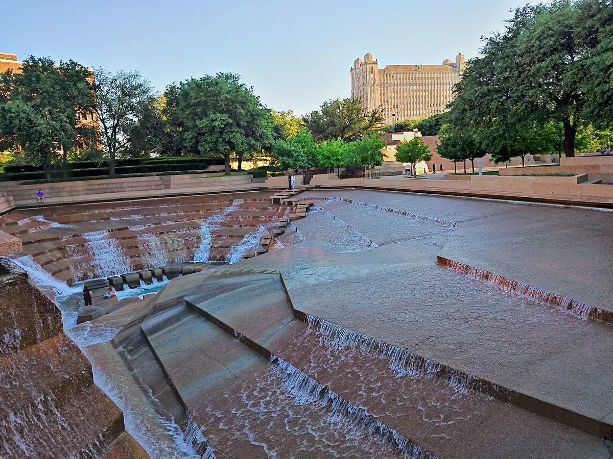 Terraced concrete steps of the Fort Worth Water Gardens with water cascading down them, downtown towers behind