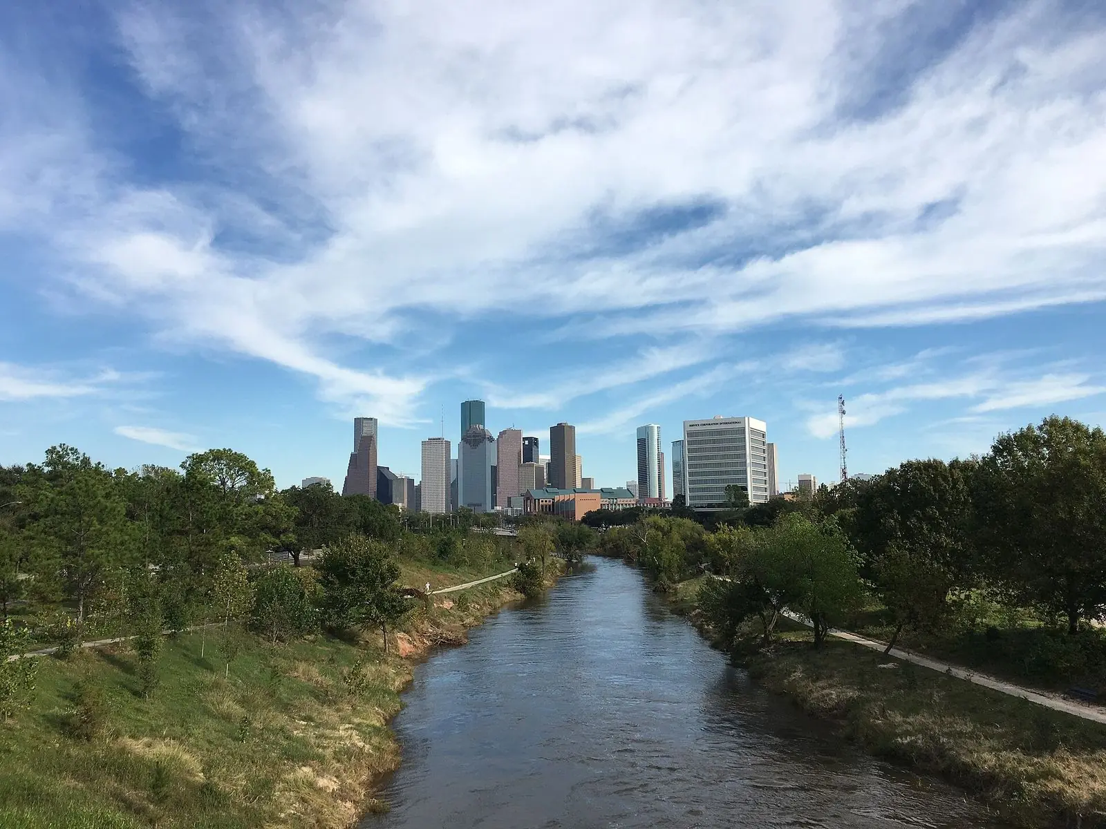 Buffalo Bayou winding between green banks toward the downtown Houston skyline, seen from the Rosemont Bridge