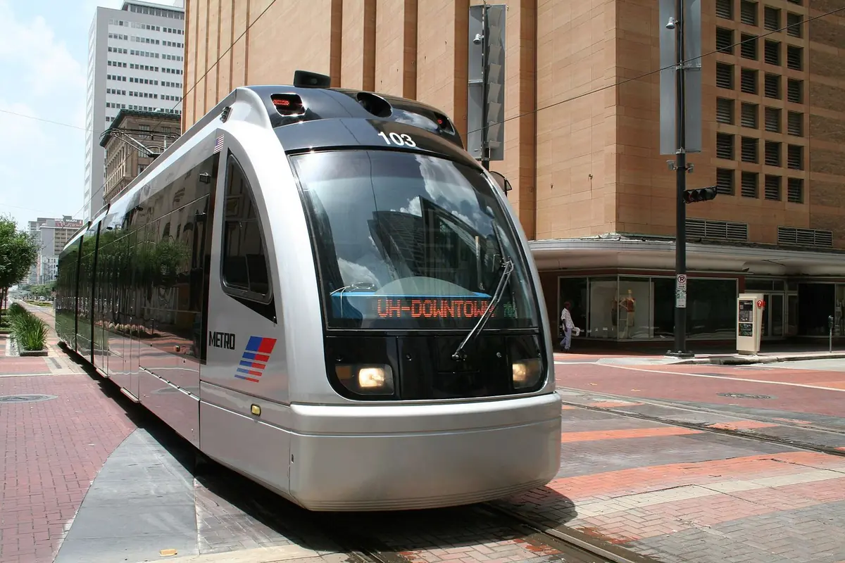 A silver METRORail train on brick-paved Main Street in downtown Houston, its sign reading UH-Downtown