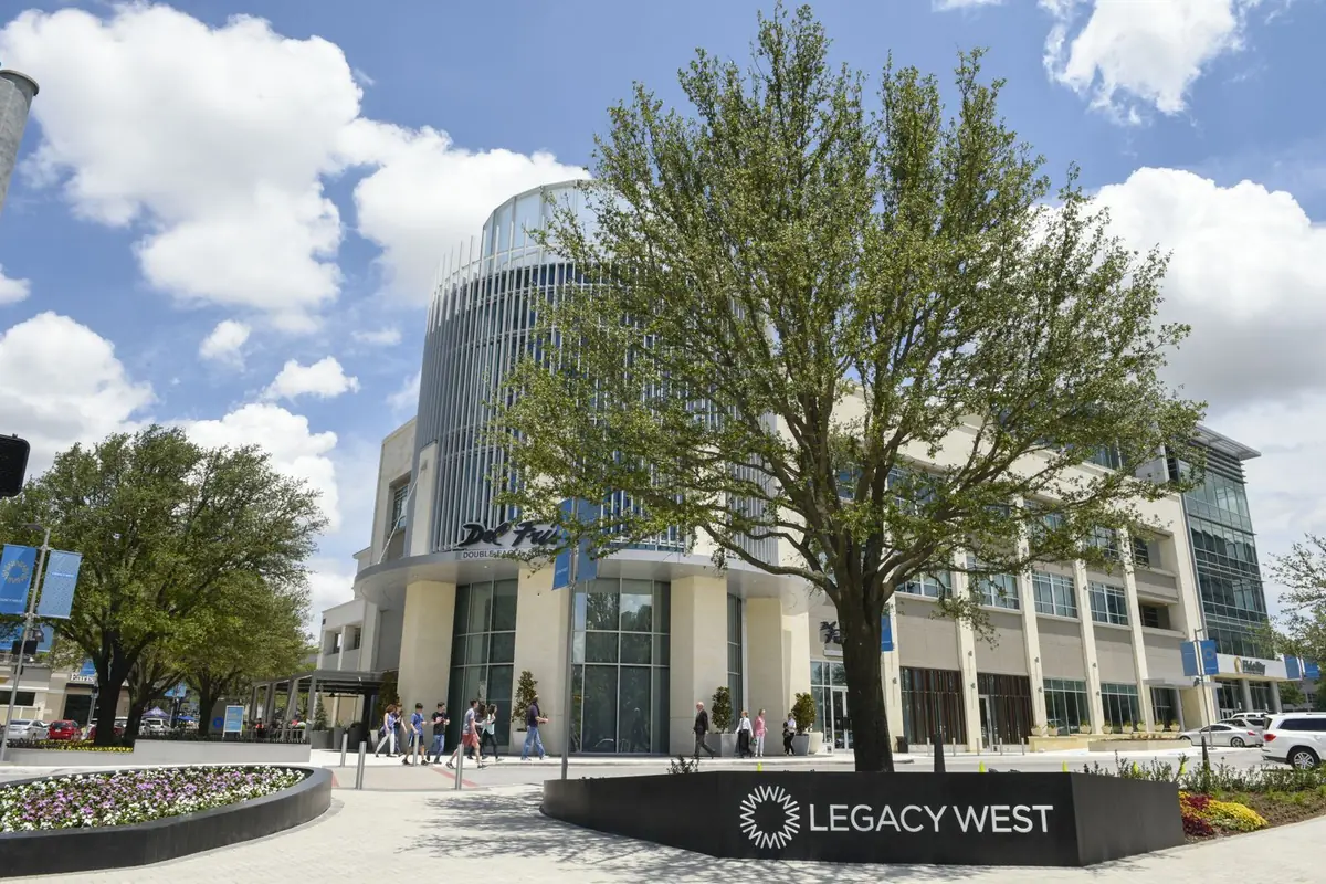 The entry to Legacy West in Plano, with its sign, a shade tree and glass office towers behind