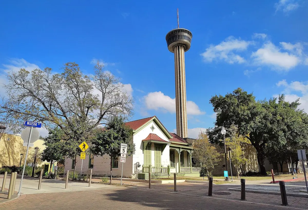 The small Kusch House in Hemisfair with the Tower of the Americas rising behind it under a blue sky