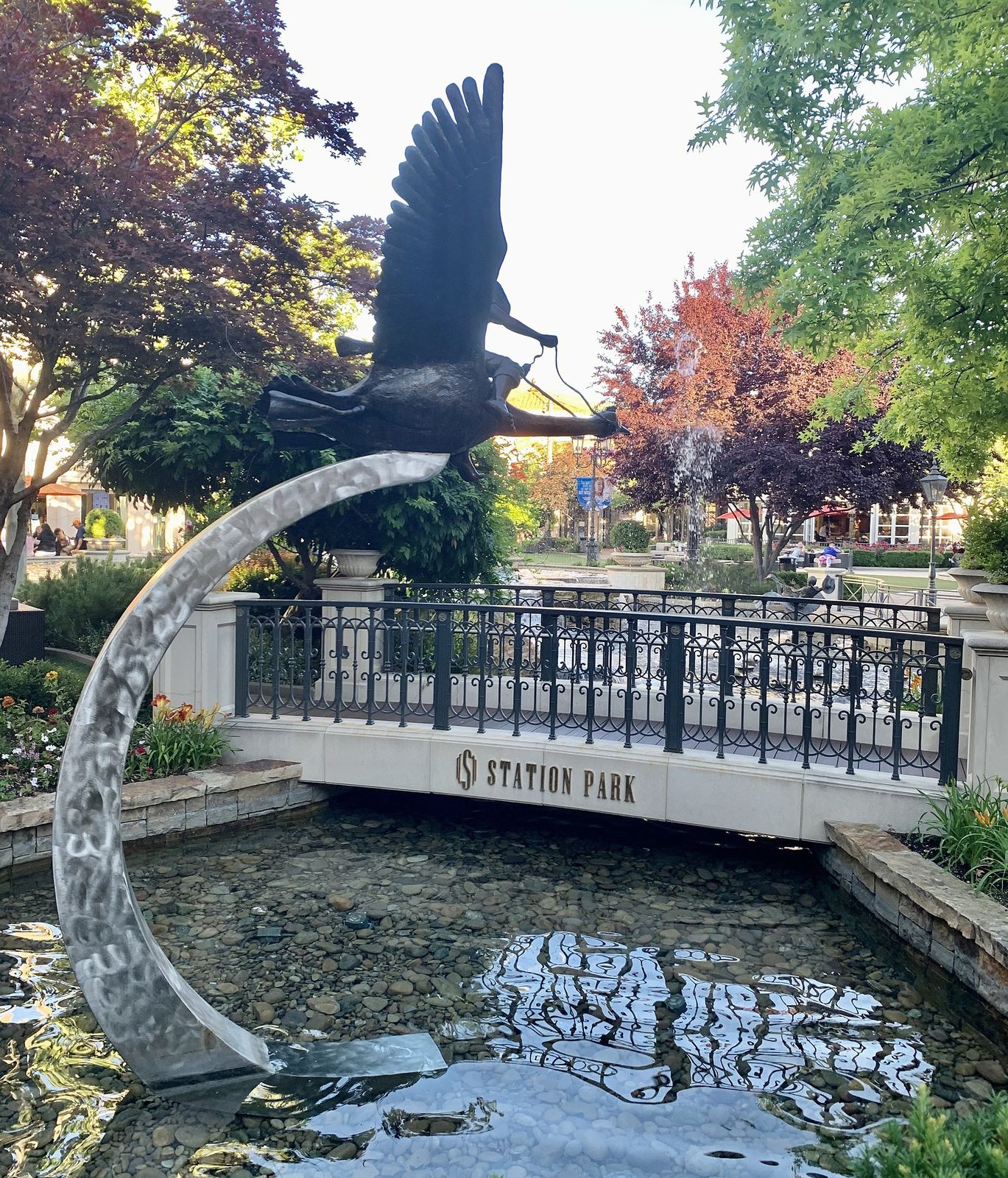 A bird sculpture above the water feature and footbridge at Station Park in Farmington