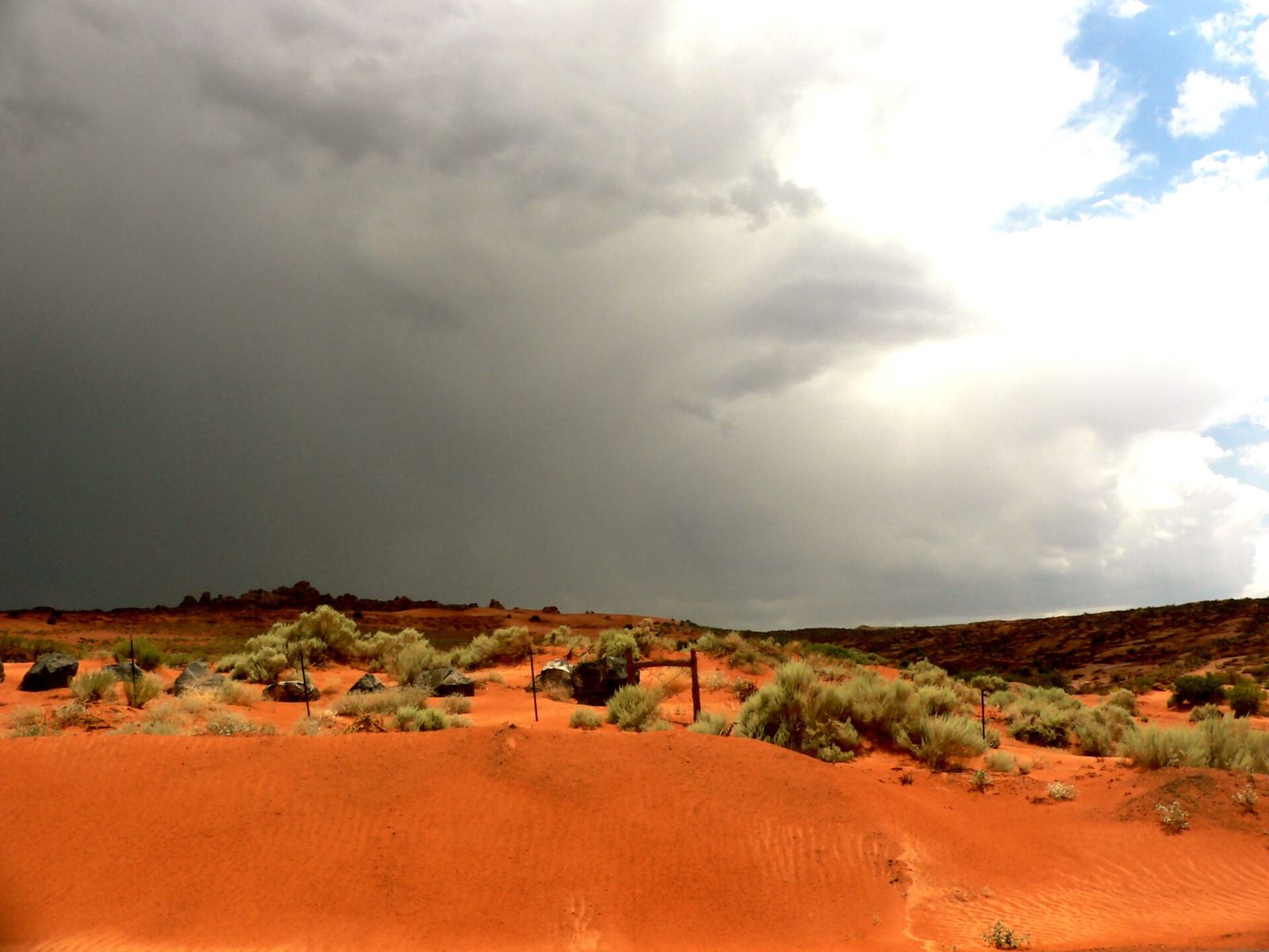 Orange sand and desert shrubs at Sand Hollow State Park under a dark, stormy sky