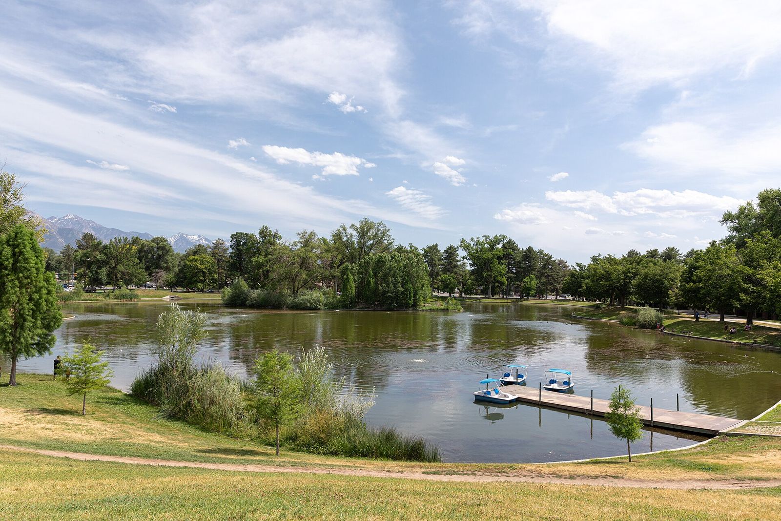 The pond at Liberty Park in summer, with pedal boats at a small dock and trees along the shore