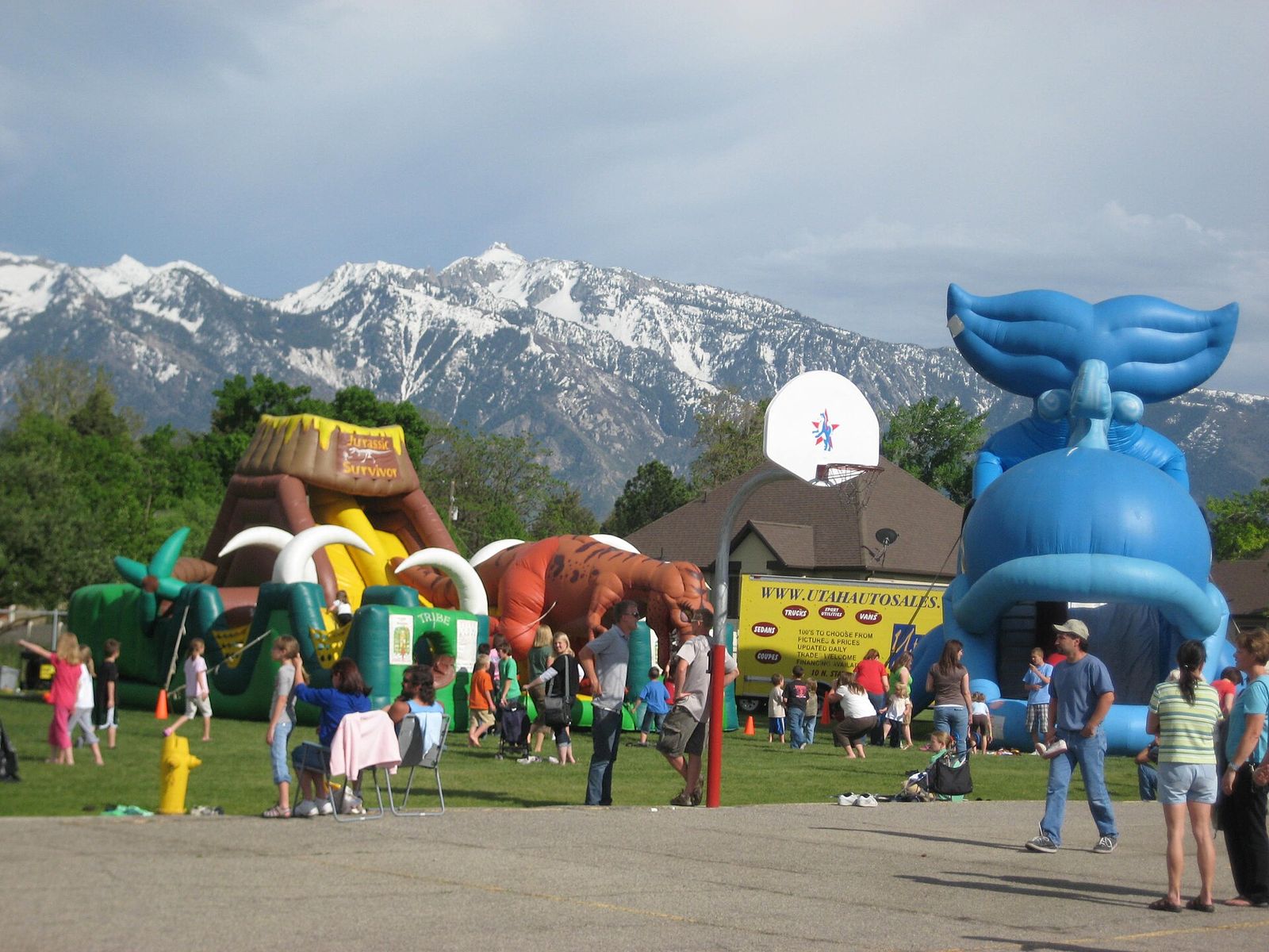 Families at a school fair with inflatable rides, snowy Wasatch peaks behind