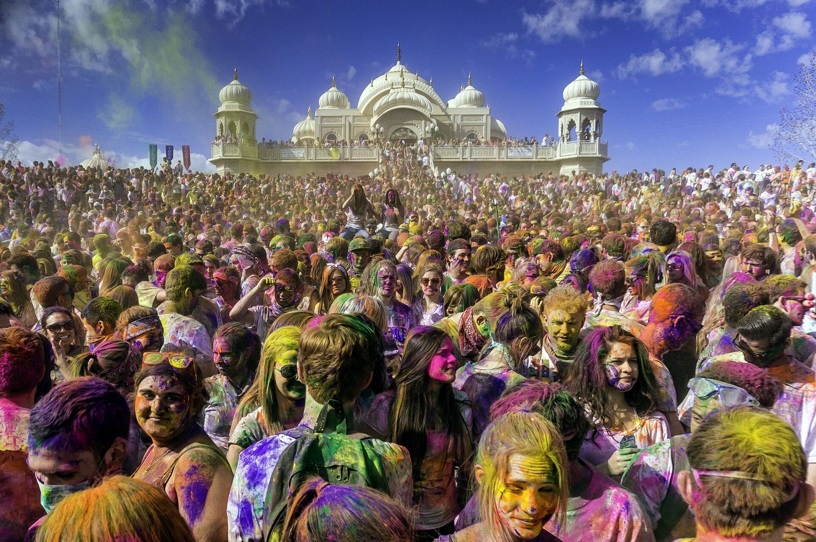A crowd covered in colored powder at the 2013 Festival of Colors, with the Sri Sri Radha Krishna Temple behind