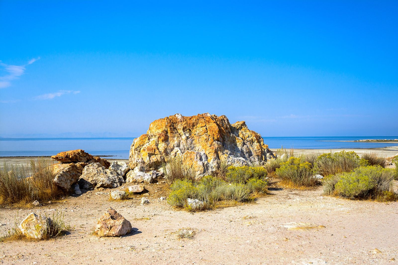 Orange-tinted rocks and brush on the shore of Antelope Island State Park under a blue sky