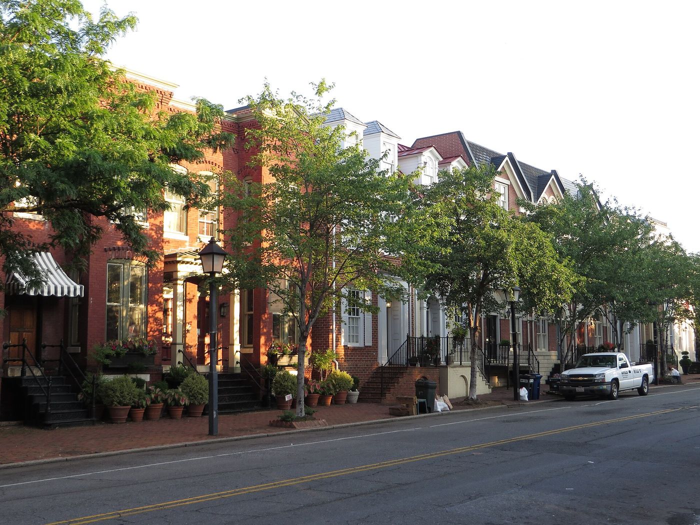 Row of brick townhouses with shade trees on an Old Town Alexandria street