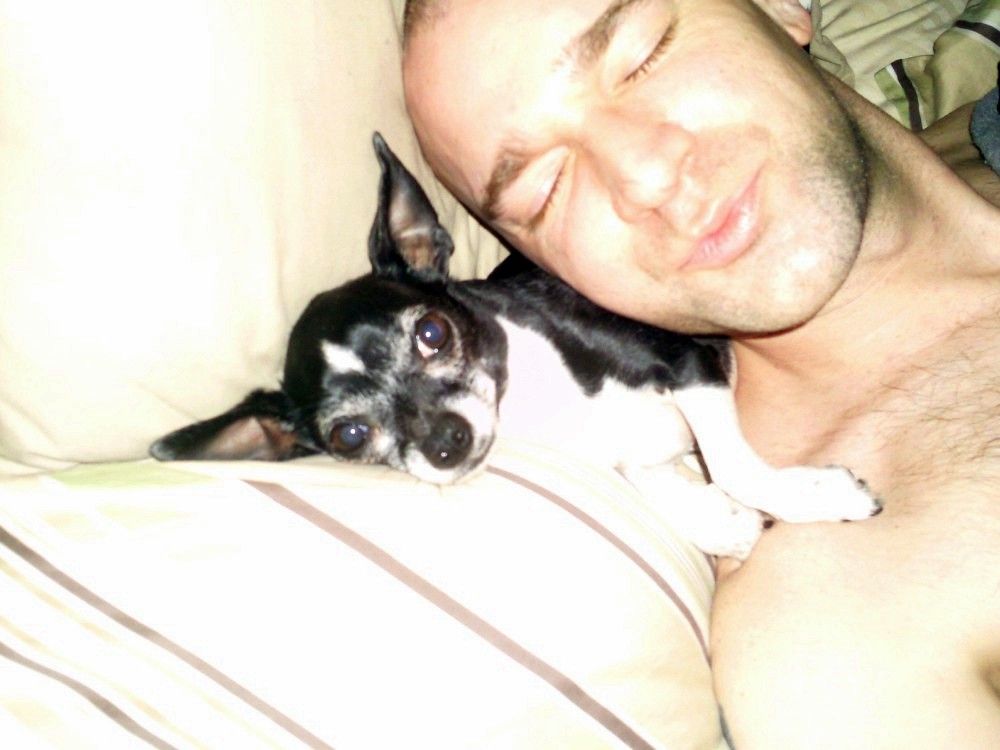 Man resting his head on a pillow next to a small black and white dog
