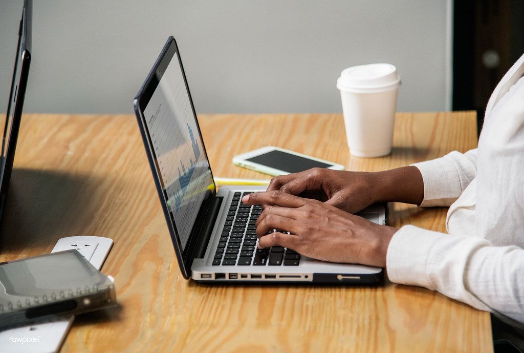 Person typing on a laptop at a wooden table beside a coffee cup and phone