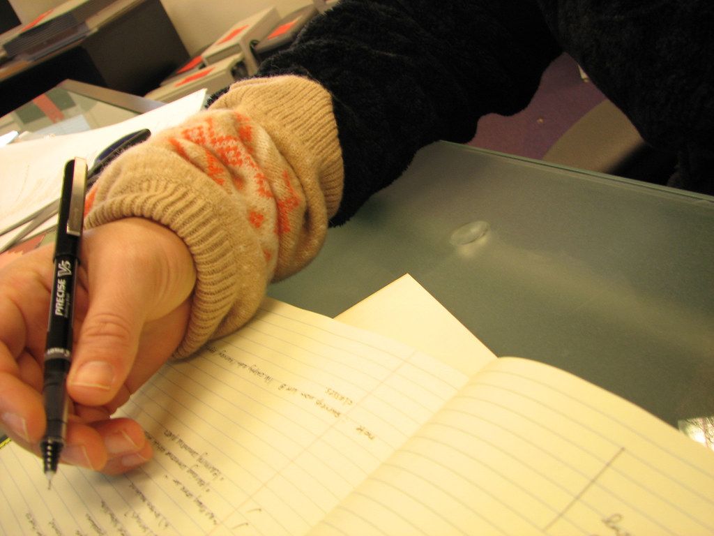 Hand in a knit sleeve writing notes with a pen in an open notebook