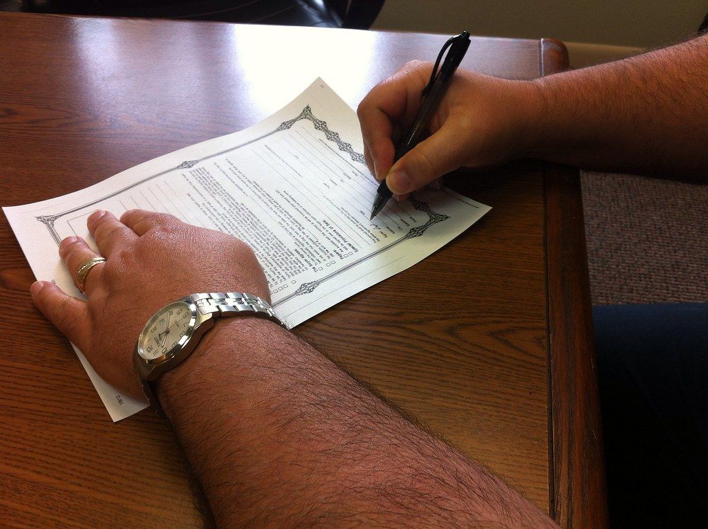Hand with a wristwatch signing a printed document on a wooden desk